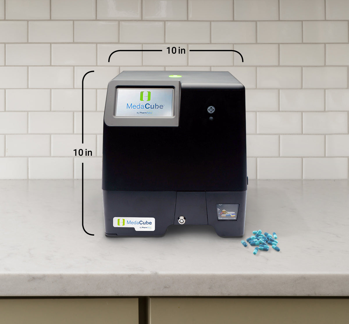 MedaCube device on counter with 10 inch measurement and 10 inch measurement across the width of the device and a 10 inch measurement on the left side of the device showing the height. Pills on counter.